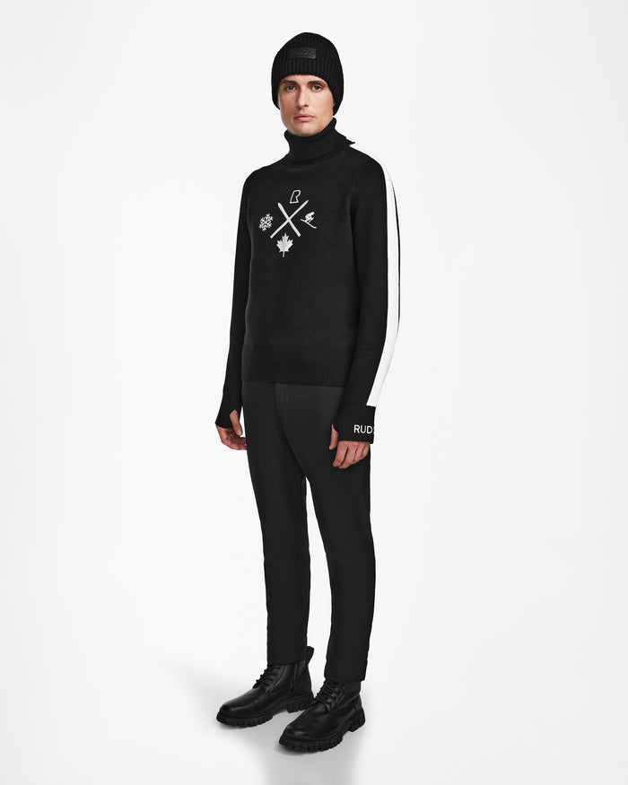 A person stands against a white background wearing the OLIVIER - 6524545 Black mens ski turtleneck by Rudsak, featuring white graphic symbols, paired with black pants with a white stripe, a black beanie, and black lace-up boots—ideal for winter style.