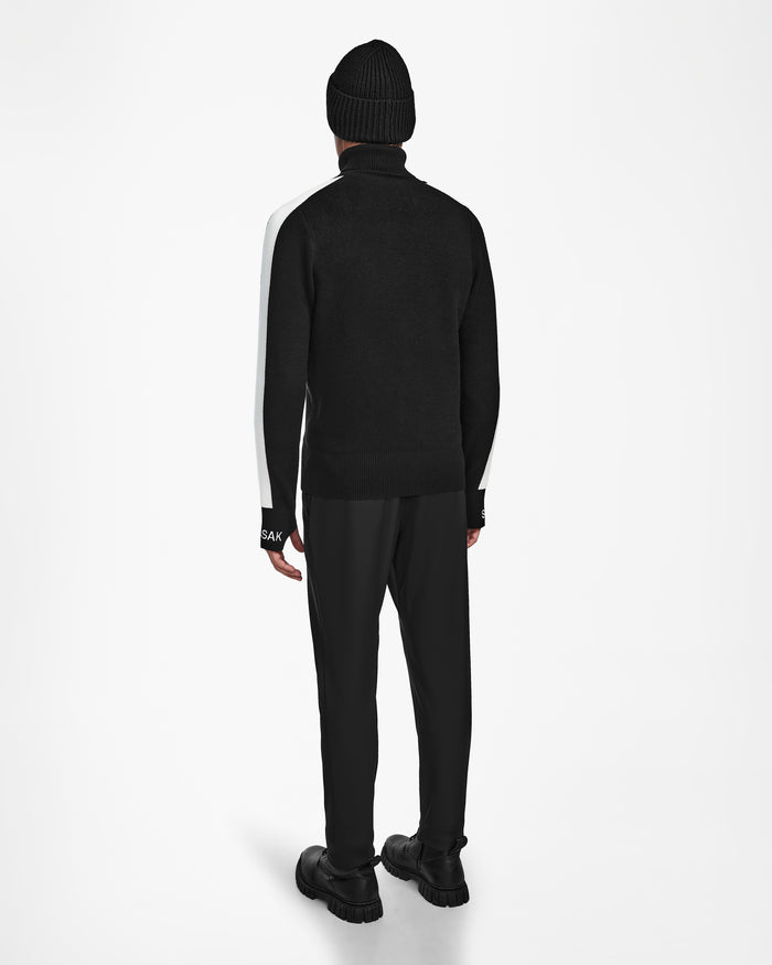 A person stands facing away, wearing the Rudsak OLIVIER - 6524545 Black jacket with white sleeves over a mens ski turtleneck and a black beanie, all set against a plain white background.