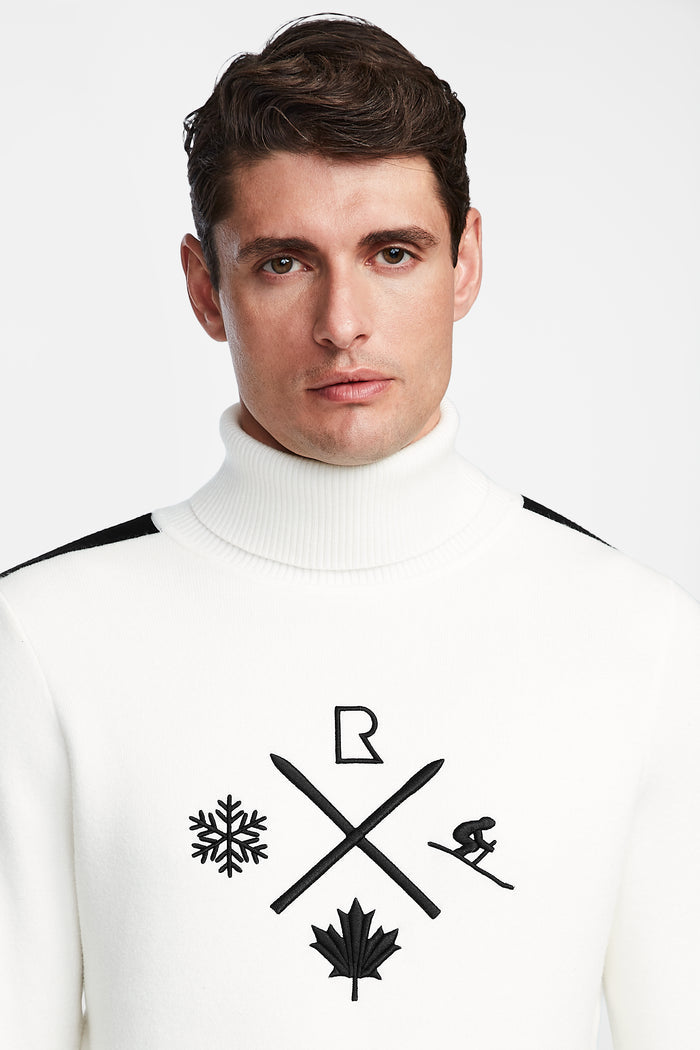 A man with short brown hair wears the OLIVIER - 6524545 Optic White men’s ski turtleneck sweater by Rudsak, featuring black symbols—snowflake, crossed skis, maple leaf, ski jumper, and letter R—ideal for winter or après-ski events.