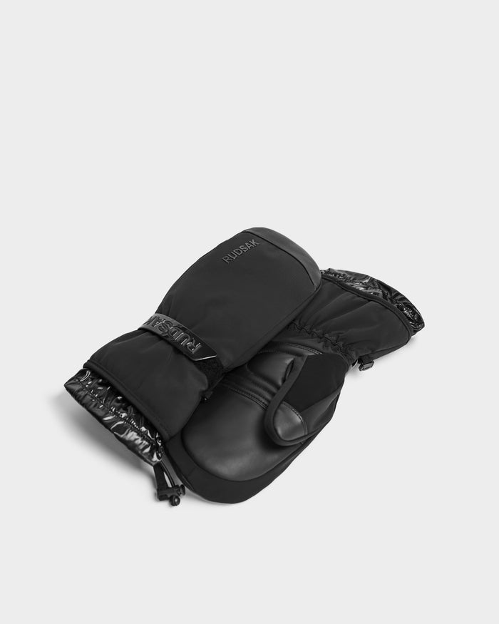 A pair of Rudsak OLTEN - 9425565 Black ski mittens with 3M Thinsulate insulation, adjustable wrist straps, and shiny trim are laid overlapping on a light gray surface.