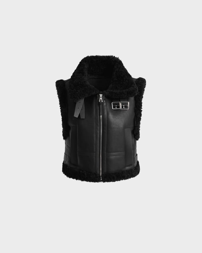 The PAISLEY - L125516 Black by Rudsak is a women’s cropped vegan leather vest with black faux shearling, a wide collar, front zipper, side buckle strap, and fleece-trimmed edges, shown on a plain white background.