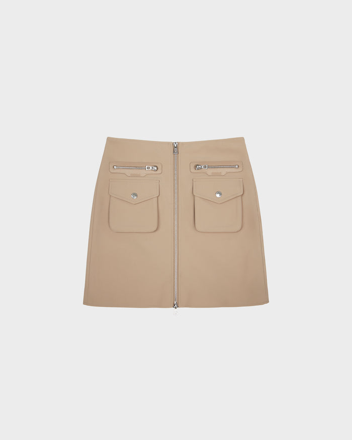 The PAMINA - 8525025 Almond by Rudsak is a beige womens vegan leather mini skirt, featuring a front zipper, utility snap-button pockets, and two horizontal zipper pockets above them, shown against a plain white background.