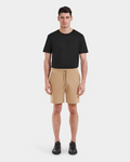A man stands facing forward in a Rudsak PASCAL - 6524022 Almond t-shirt, casual drawstring shorts, and black sneakers against a plain white background.