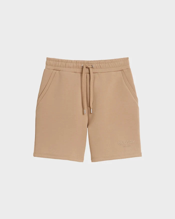 The PASCAL - 6524022 Almond mens jersey shorts by Rudsak feature side pockets, a stretch waistband, and RUDSAK embroidery on the lower left leg from the BASE Collection, shown on a plain white background.