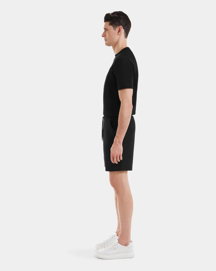 A man in profile faces right, wearing a black PASCAL - 6524022 t-shirt by Rudsak, mens double jersey shorts with a stretch waistband, and white sneakers, all set against a plain white background.