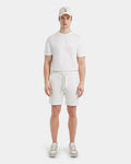 A person stands facing forward in the Rudsak PASCAL - 6524022 ICELAND men’s jersey shorts with a stretch waistband, paired with a white cap, white short-sleeve shirt, and beige and white sneakers against a plain white background.