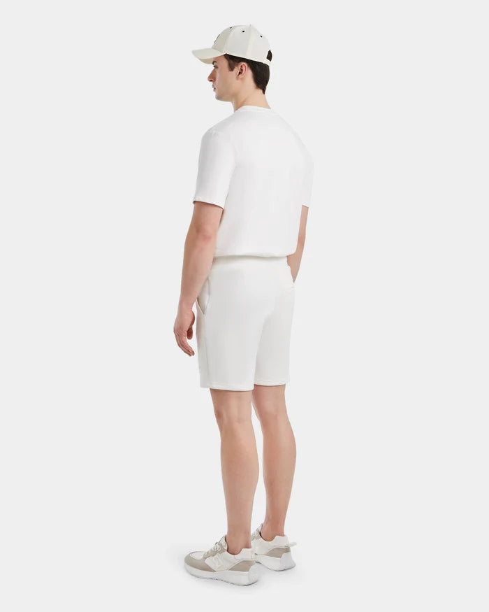 A man faces away, wearing a white cap, short-sleeve shirt, Rudsak PASCAL - 6524022 ICELAND mens jersey shorts with a stretch comfort waistband, and white sneakers with beige accents against a plain white background.