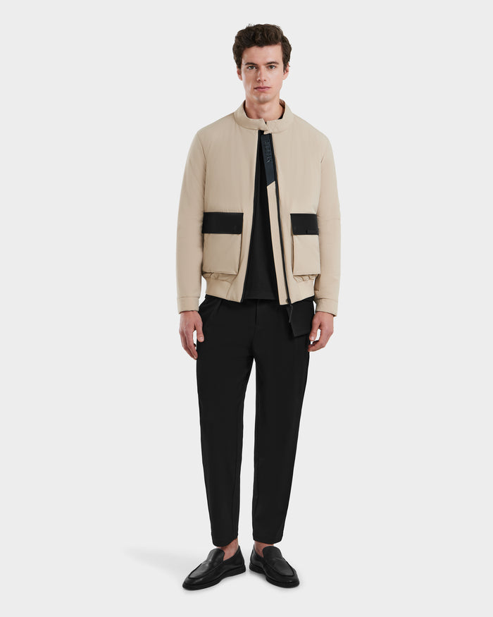 A man faces forward against a plain white background, wearing the Rudsak PETER - 6125001 Almond bomber jacket with modern vegan leather accents, paired with a black shirt, black pants, and black loafers.