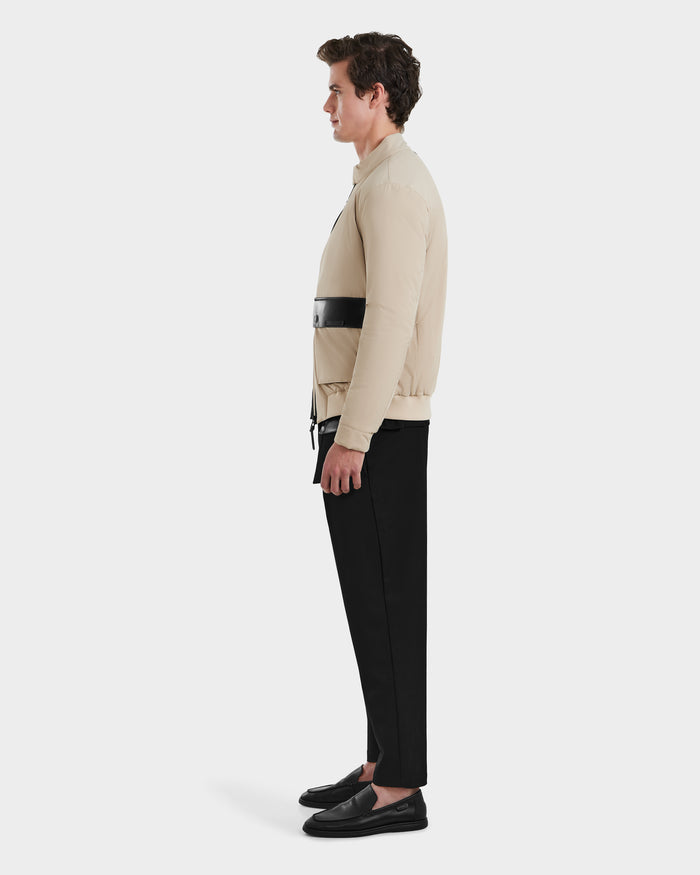A man in profile wears the Rudsak PETER - 6125001 Almond bomber jacket—beige with a black horizontal stripe—paired with black pants and slip-on shoes against a plain white background.