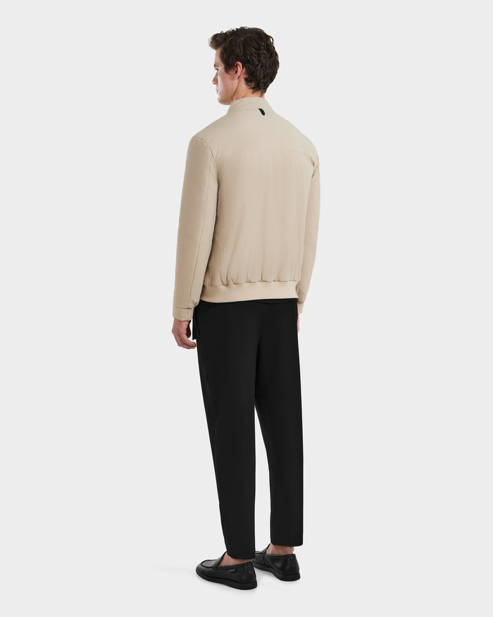 A man faces away wearing Rudsaks PETER - 6125001 Almond lightweight bomber with vegan leather accents, paired with black pants and shoes, against a plain white background.