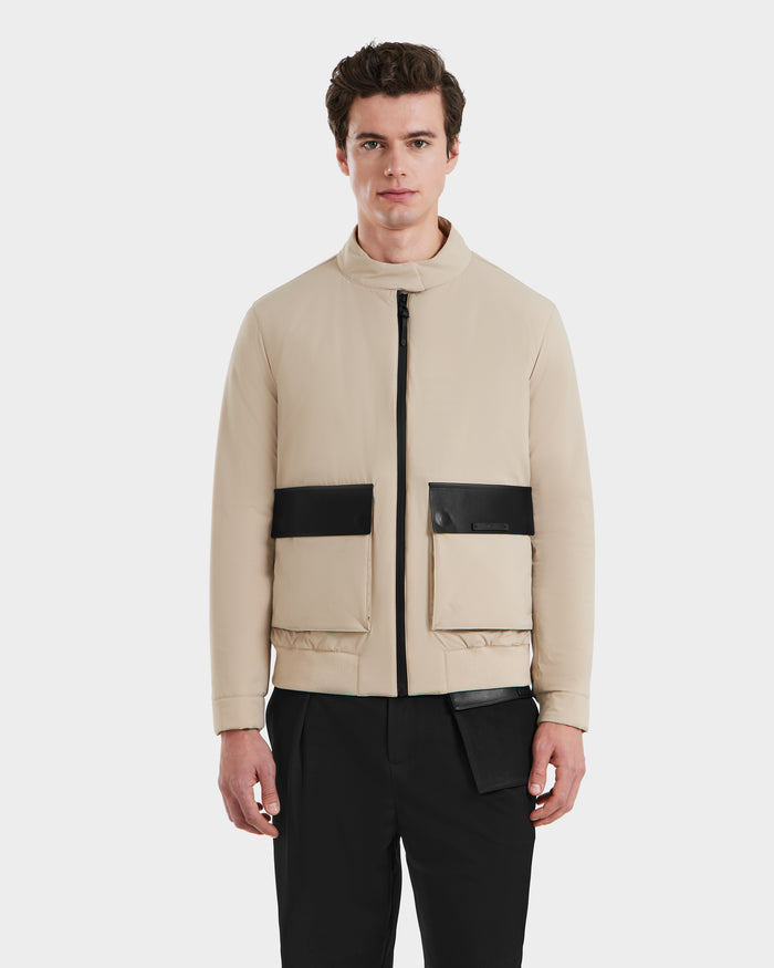 A man wears the Rudsak PETER - 6125001 Almond bomber jacket with black rectangular vegan leather-accented pockets, paired with black pants, standing against a plain white background.