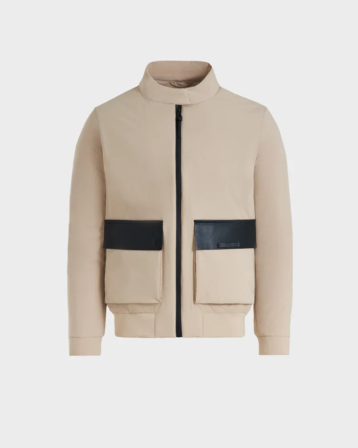 The Rudsak PETER - 6125001 Almond is a lightweight beige bomber jacket with a high collar, front zipper, and two large beige pockets with black flaps, featuring modern design details and vegan leather accents against a white background.