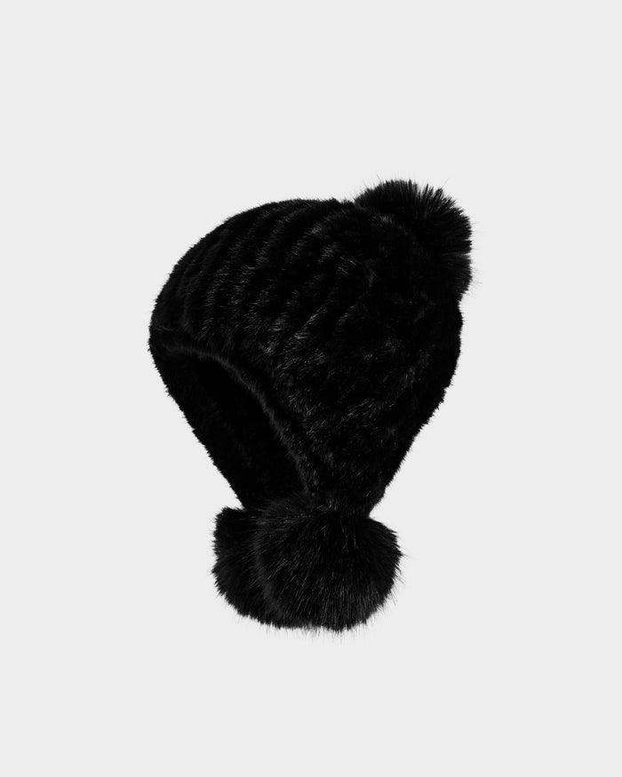 The Rudsak PIA - 8425547 Black women’s faux fur hat features a ribbed texture and two large pom-poms—one on top, one at the end of an earflap—creating a cozy winter accessory shown against a plain light background.