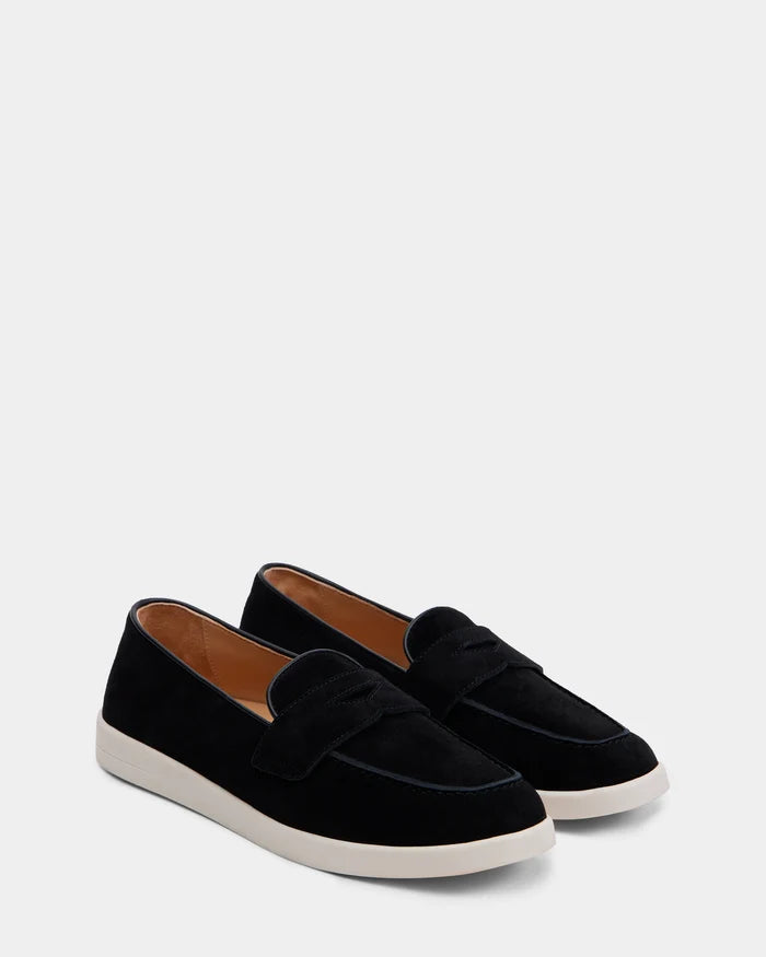 The Rudsak RABECCA - 8225006 Black womens luxury slip-on loafers, featuring black suede, white rubber soles, and brown inner lining, are displayed on a light gray background.
