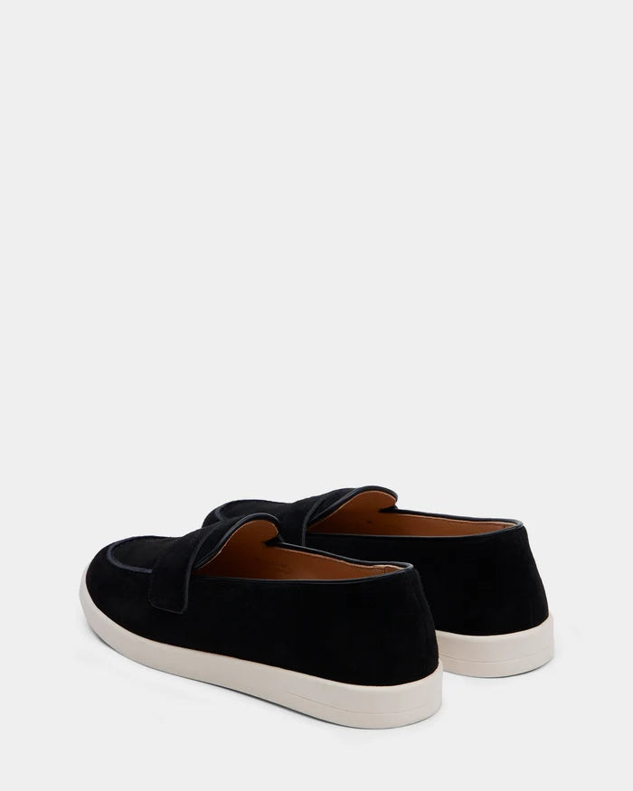 The Rudsak RABECCA - 8225006 Black suede loafer slip-ons, featuring white rubber soles, are displayed from the back at a slight angle against a plain white background.