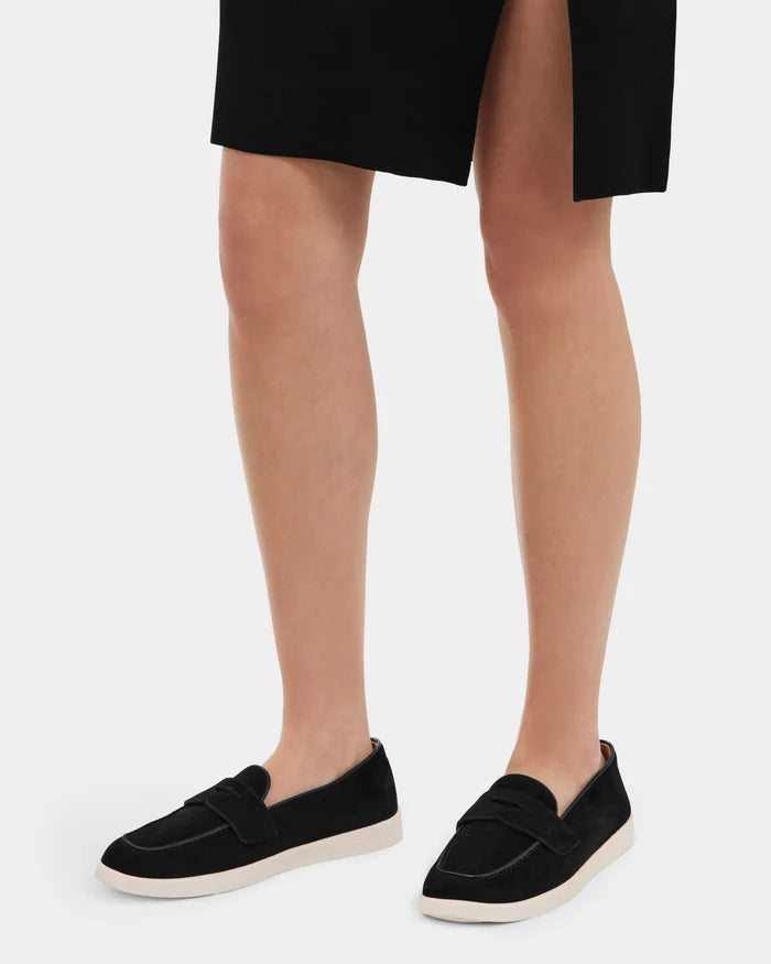 A person wearing a Rudsak RABECCA - 8225006 Black skirt with a front slit and chic women’s luxury loafers with white soles stands against a plain white background.