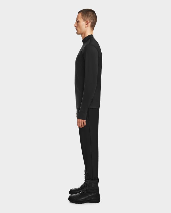 A person stands in profile facing left, wearing the RALI - 6524522 Black men’s active top by Rudsak, paired with black pants and boots against a plain light gray background.