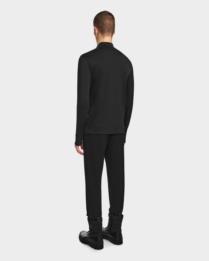 A man faces away from the camera wearing the Rudsak RALI - 6524522 Black men’s active top, paired with black pants and boots—ideal for layering—against a plain light gray background.