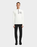 A man stands facing forward wearing the Rudsak RALI - 6524522 Optic White long-sleeve zip-up shirt with black text on the chest, paired with black pants and boots, against a plain light background.