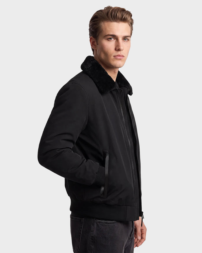 A man with short brown hair wears the Rudsak REECE - 6124592 Black men's bomber jacket with a shearling collar, standing sideways and looking at the camera against a plain light background.