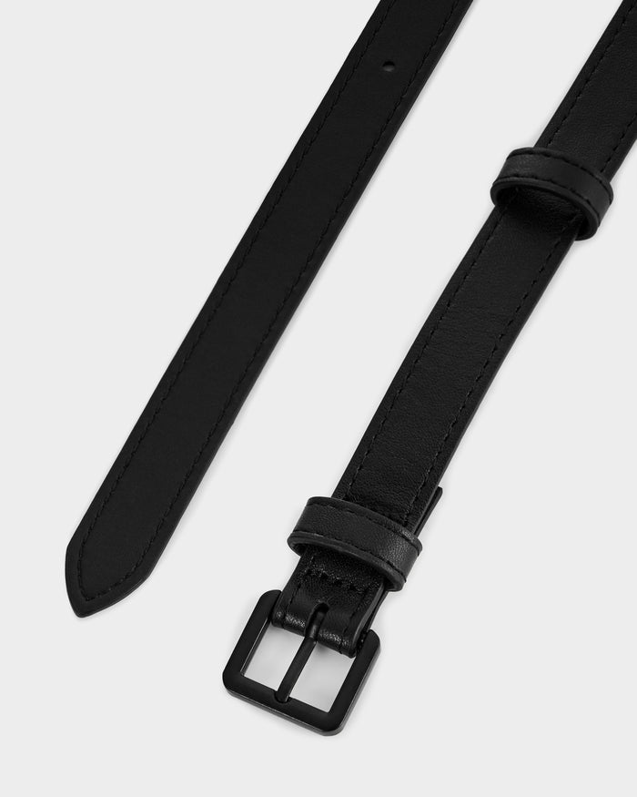 A close-up of the RENA - 8425039 Black women's leather waist belt by Rudsak, featuring a matte black buckle, stitched edges, and a pointed end, set against a plain white background.