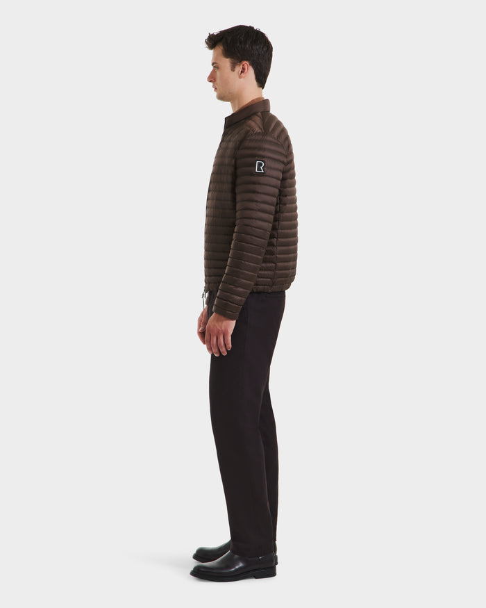 A man in profile faces left, wearing the Rudsak REYMOND M - M125523 Mocha dark brown men’s down jacket made from recycled nylon, paired with black pants and shoes against a plain white background.