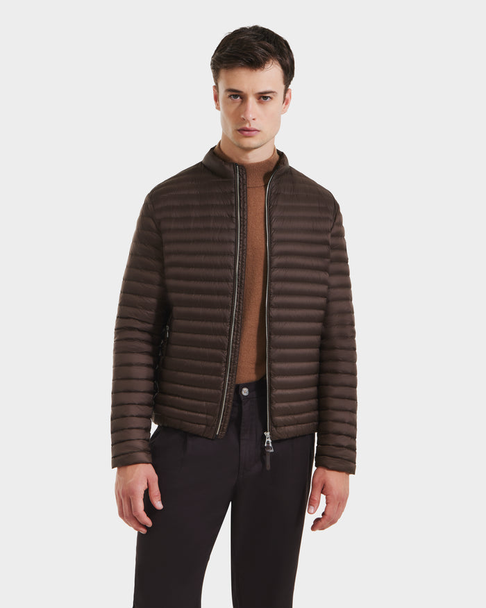 A man wearing a Rudsak REYMOND M - M125523 Mocha men’s puffer jacket stands over a tan sweater and black pants against a plain white background.