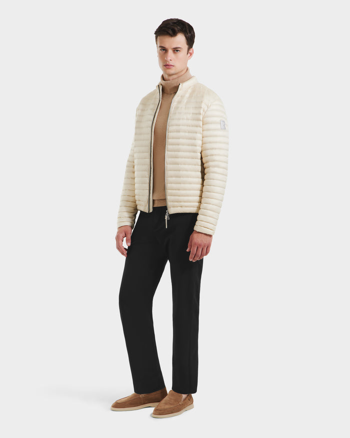 A man stands against a plain white background wearing the Rudsak REYMOND M - M125523 Vanilla RDS-certified down quilted jacket over a beige turtleneck, with black pants and brown slip-on shoes.