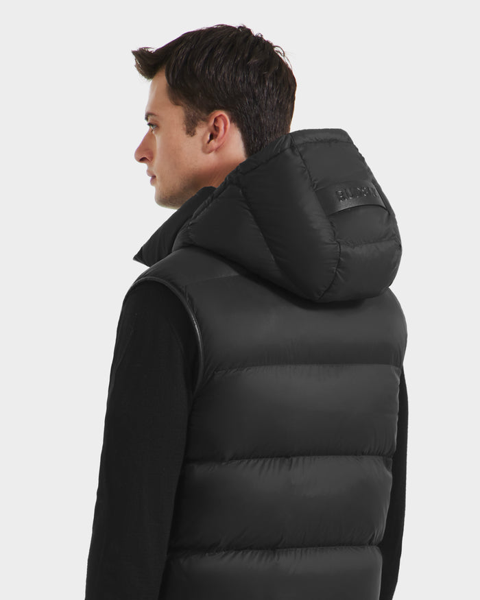A man with short brown hair wears the Rudsak RICHARDSON - M125527 Black water-repellent men’s hooded vest over a black long-sleeve shirt, facing slightly left against a plain light background.