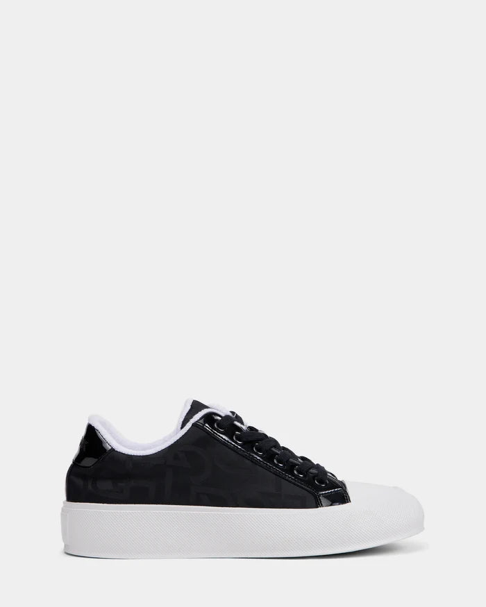 The Rudsak RIMA - 8225001 Black Pattern is a black monogram print sneaker featuring a white rubber sole and toe cap, black laces, and subtle logo detailing on the side, shown against a plain white background.