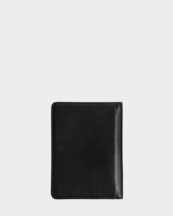 The ROBIN - 9425562 Black by Rudsak is a closed black leather passport holder with clean stitching, displayed upright against a light gray background—ideal as a unisex travel wallet.