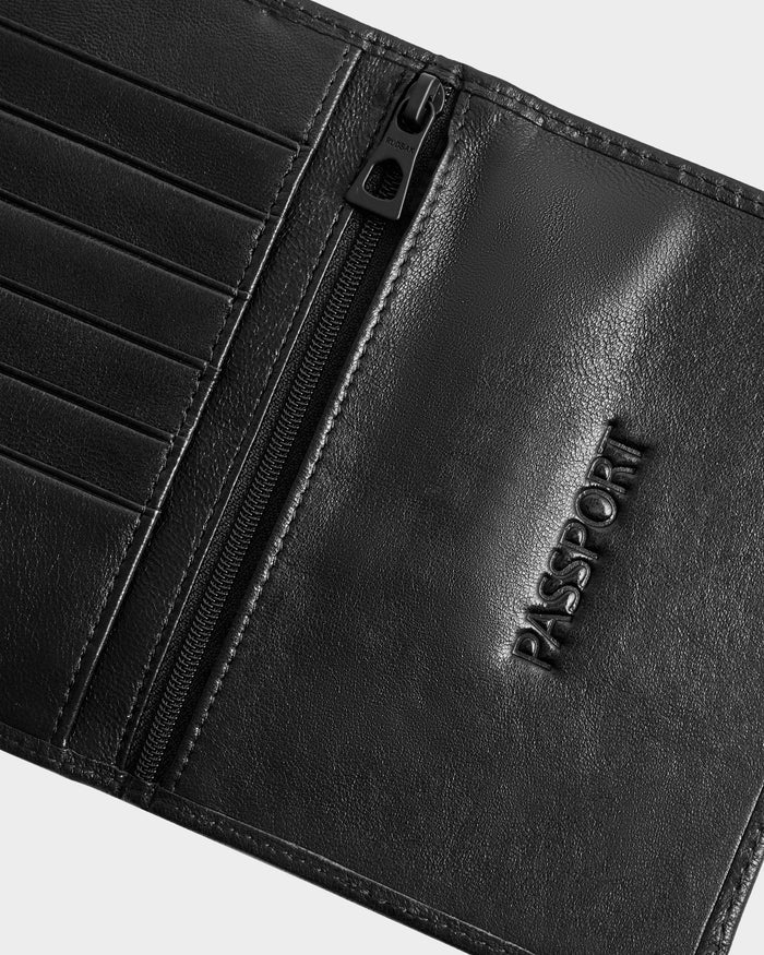 A close-up of the Rudsak ROBIN - 9425562 Black leather passport holder, a unisex design featuring card slots, a zippered pocket, and PASSPORT embossed on the right side.
