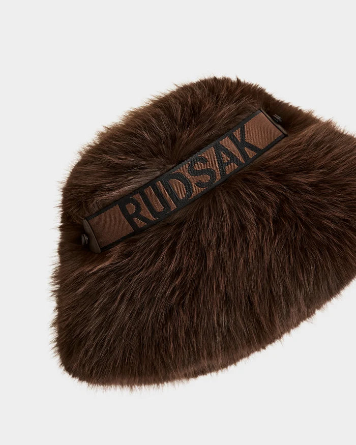The ROMINA - 8425545 Espresso by Rudsak is a brown faux fur bag with a thick strap displaying "RUDSAK" in bold black letters. Its soft, fluffy texture makes it a standout winter accessory, shown against a white background.