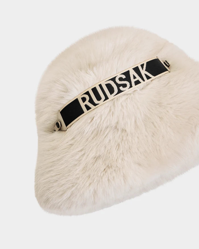 The Rudsak ROMINA - 8425545 Vanilla is a white faux fur bucket hat with a black strap featuring bold white RUDSAK lettering—an ultra-cozy, luxe women’s winter accessory shown on a plain white background.