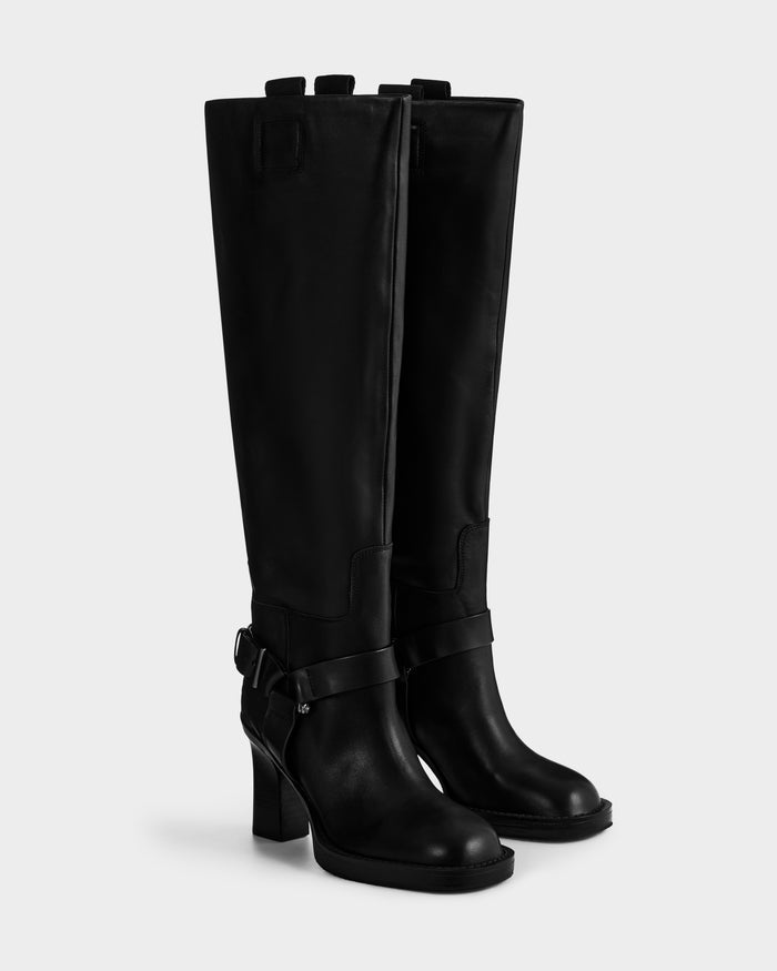 The ROSSEY - 8225574 Black boots by Rudsak are tall black leather heeled boots featuring decorative straps and buckles at the ankle, displayed on a plain white background.