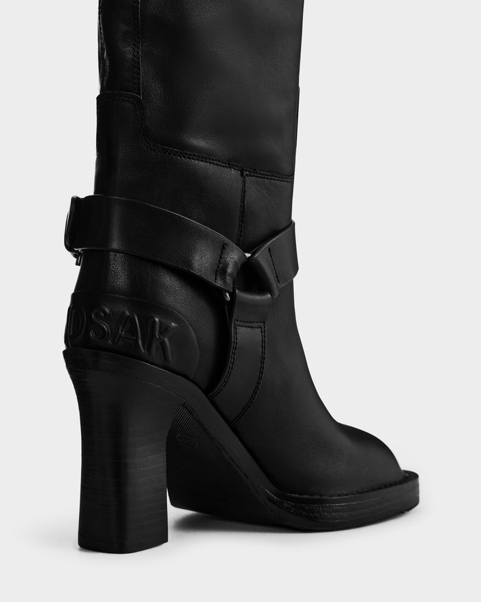 Close-up of the Rudsak ROSSEY - 8225574 Black leather heeled boot, featuring a decorative strap and embossed text near the heel, displayed against a plain light background.