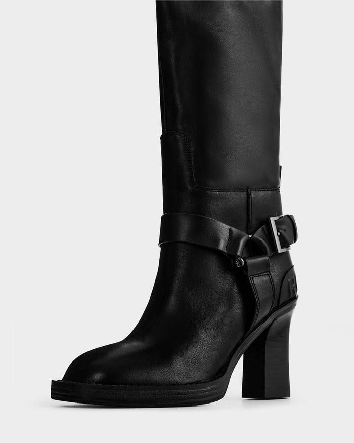 The ROSSEY - 8225574 Black by Rudsak is a black leather high-heeled boot with a rounded toe and an ankle strap featuring a silver buckle.