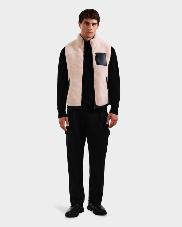 A man stands facing forward, wearing the Rudsak RUMMY - U524502 Vanilla M polar fleece vest with a black chest pocket over a black outfit against a plain light gray background.