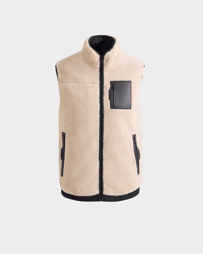 The Rudsak RUMMY - U524502 Vanilla M is a beige unisex teddy vest with black trim, two zippered side pockets, and a black zippered chest pocket, shown against a plain light gray background.