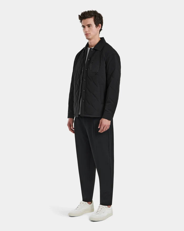 A man stands against a plain background wearing the RYAN - 6125023 Black quilted jacket by Rudsak, paired with matching black pants, a white t-shirt, and white sneakers.
