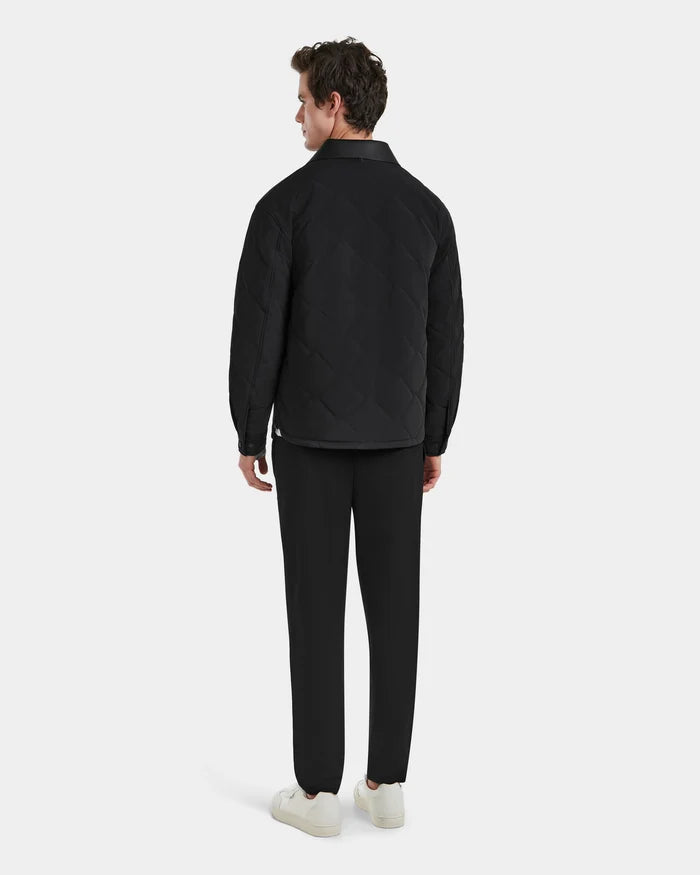 A man faces away, wearing the Rudsak RYAN - 6125023 Black quilted light jacket with eco-friendly insulation, paired with black pants and white sneakers, set against a plain light gray background.