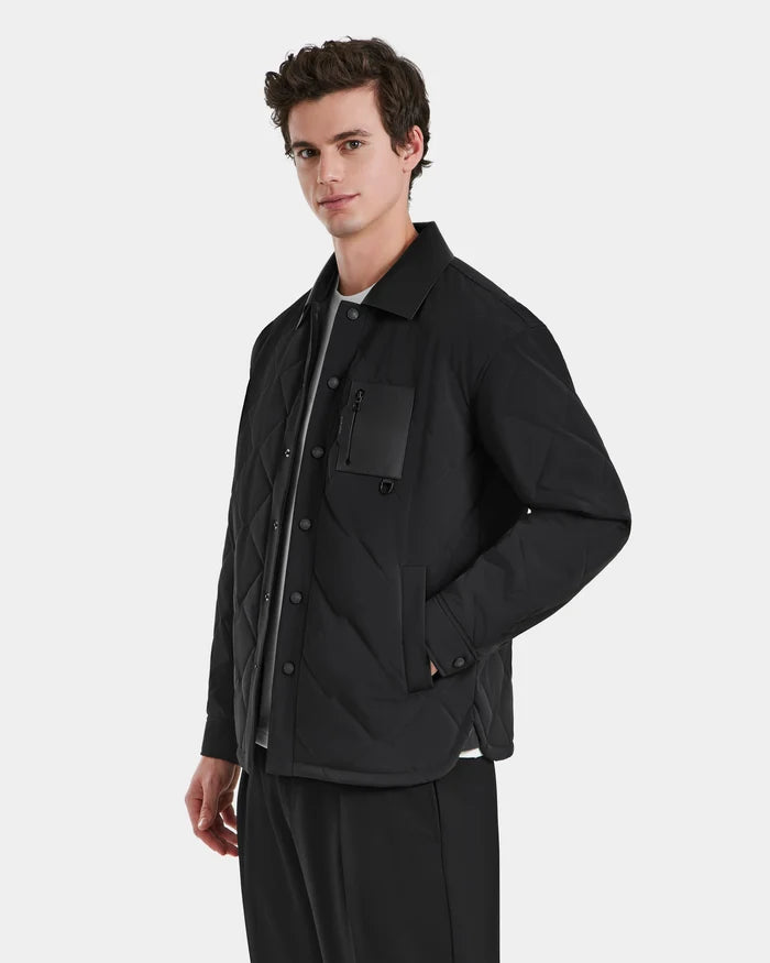A modern man wears the RYAN - 6125023 Black quilted jacket by Rudsak, made with eco-friendly insulation and featuring a chest pocket and side pockets, over a gray shirt against a plain white background.