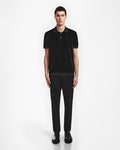 A young man stands against a white background, wearing the Rudsak SAM - 6524502 Black polo with black pants and shoes, his arms relaxed at his sides for a modern luxury mens look.