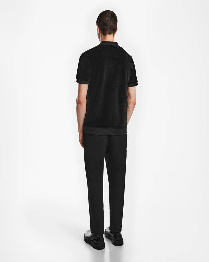 A man faces away from the camera wearing Rudsak’s SAM - 6524502 Black, paired with black pants and shoes against a plain white background—a refined take on luxury men’s fashion.