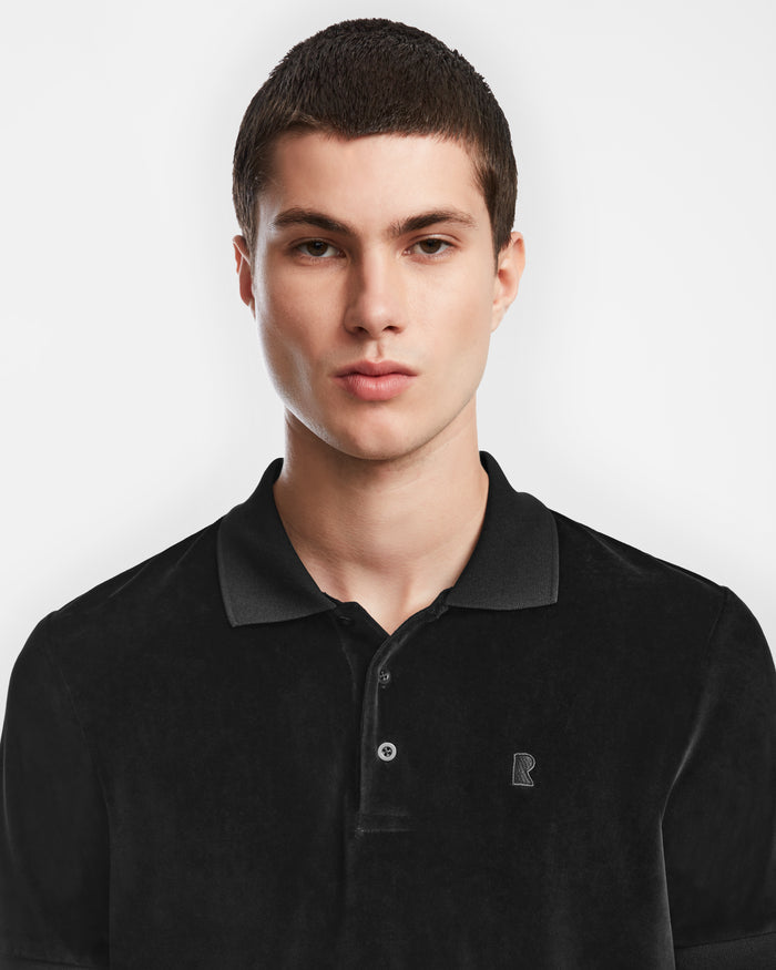A young man with short brown hair wears the Rudsak SAM - 6524502 Black polo, standing against a plain white background and looking directly at the camera with a neutral expression.