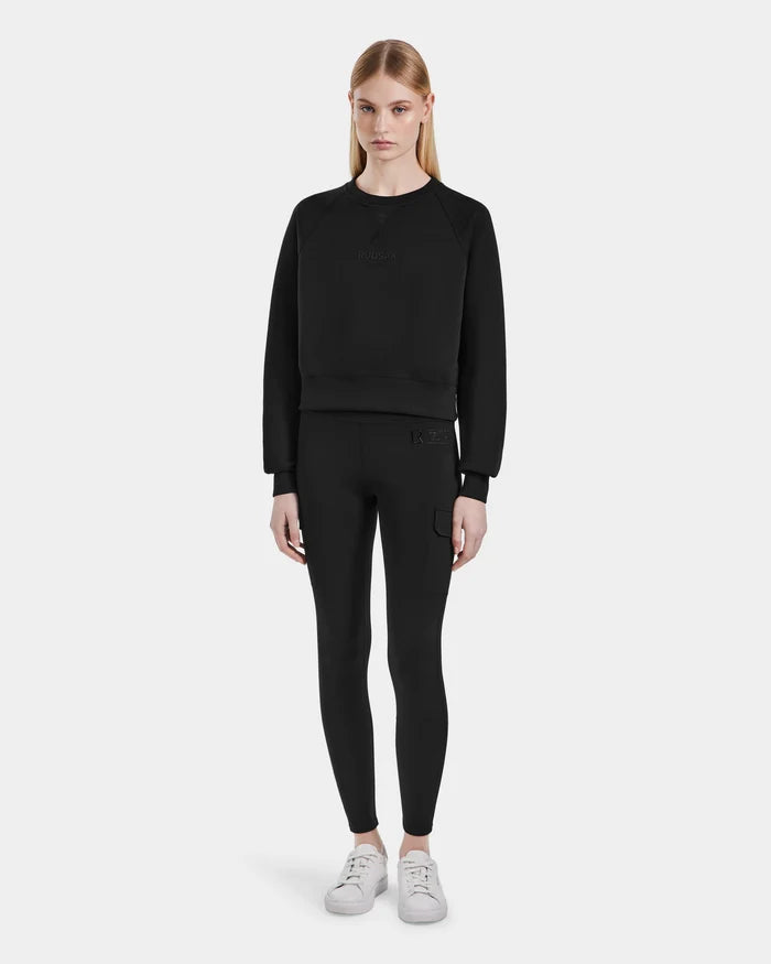 A woman with straight blonde hair and a neutral expression stands facing forward in Rudsaks SIEN - 8525090 Black long-sleeve sweatshirt and black high-rise leggings with side pockets, paired with white sneakers against a plain white background.