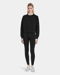 A woman with straight blonde hair and a neutral expression stands facing forward in Rudsaks SIEN - 8525090 Black long-sleeve sweatshirt and black high-rise leggings with side pockets, paired with white sneakers against a plain white background.