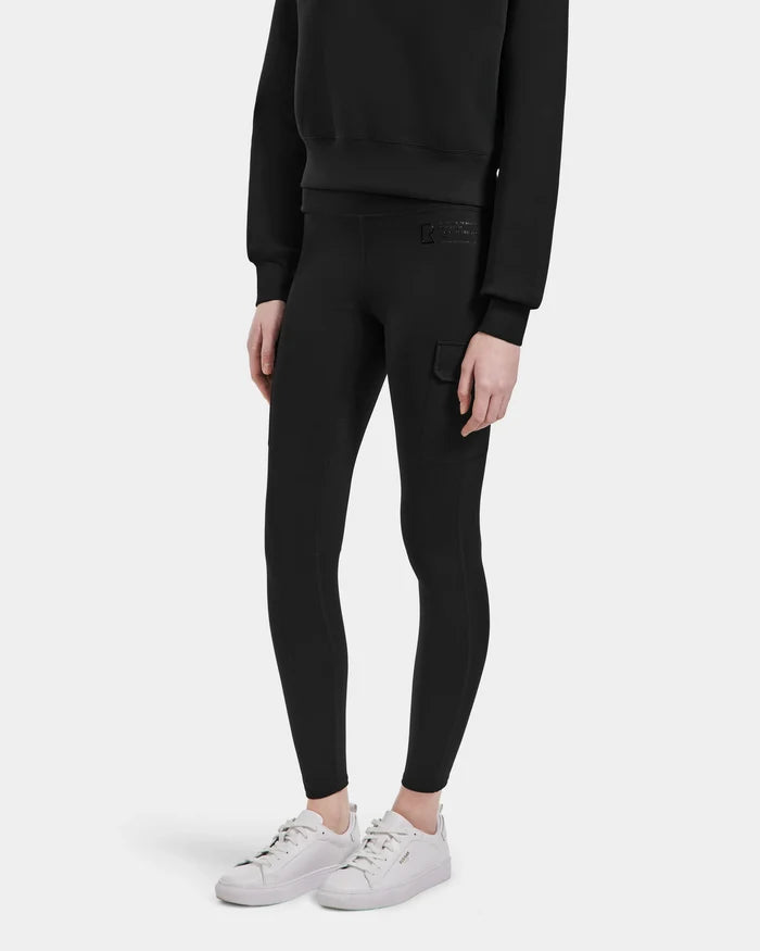 A person wearing the SIEN - 8525090 Black sweatshirt by Rudsak and luxe stretch leggings with a side pocket, paired with white sneakers, stands against a plain white background.