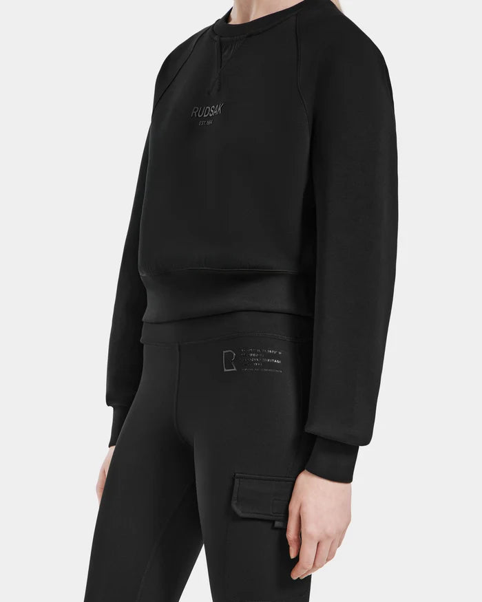 Wearing the Rudsak SIEN - 8525090 Black sweatshirt and matching high-rise leggings with side pocket and subtle logo, this minimal, sporty outfit features stretch fabric for a sleek activewear look against a plain white background.