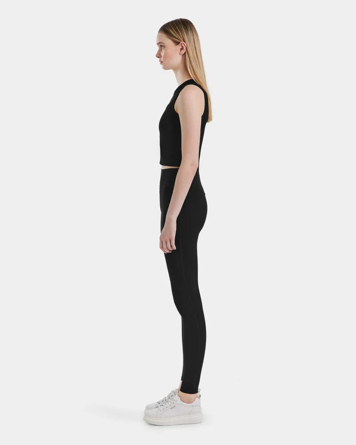 A woman stands in profile against a plain white background, wearing a black sleeveless crop top, Rudsak SONOMA - 8525071 Black leggings, and white sneakers.